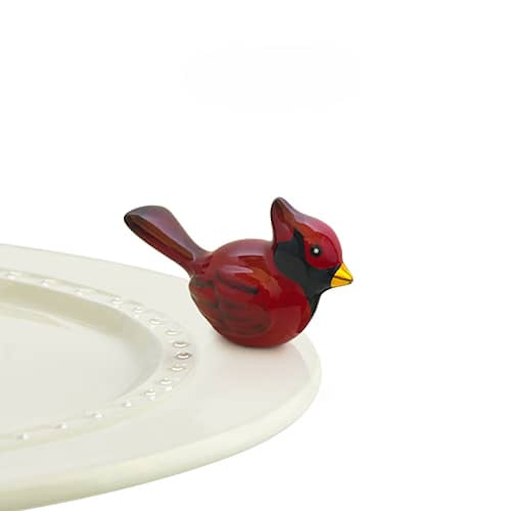 A small ceramic red cardinal figurine attached to the rim of a white serving platter.