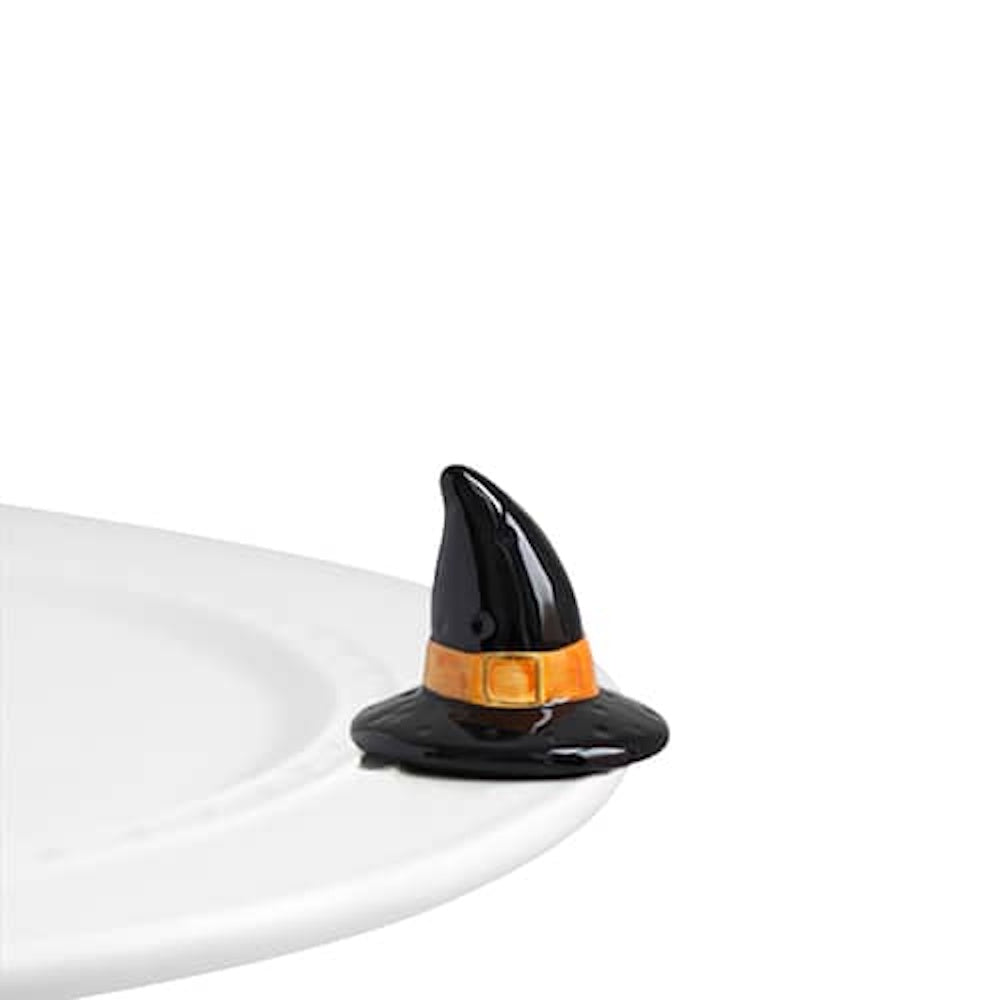 A small ceramic witch hat figurine with an orange band, attached to the edge of a white serving platter.