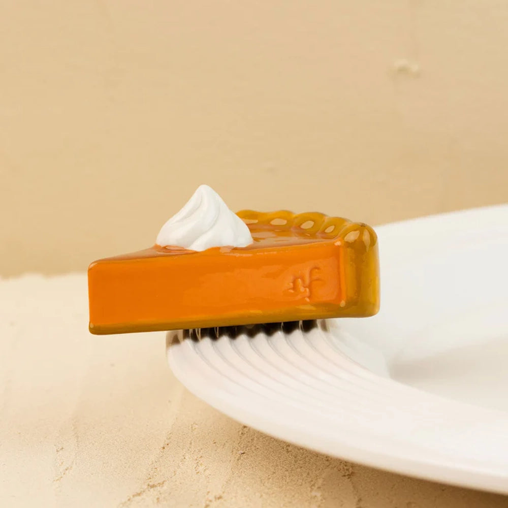 Small ceramic pumpkin pie slice figurine with a dollop of whipped cream on a white plate rim.