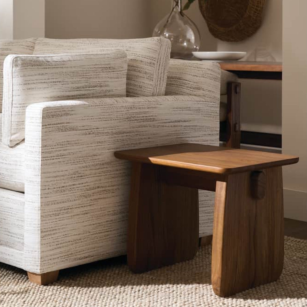 Modern walnut end table styled beside a textured armchair, showcasing sculptural panel legs and clean contemporary design.