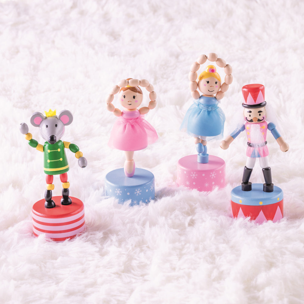 Nutcracker character wooden push puppets, including mouse and ballerina figures, on a soft white faux fur background.