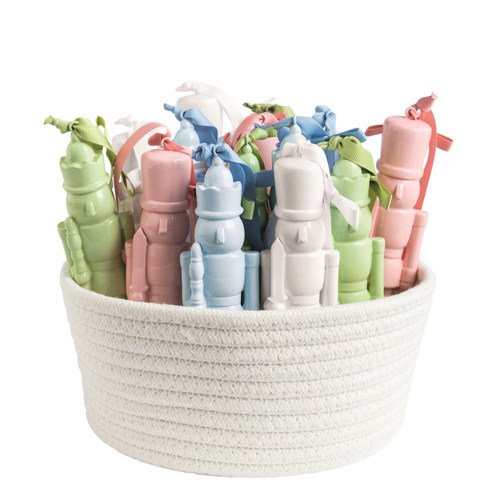 Pastel lacquered nutcracker ornaments with ribbon ties stored in a woven white rope basket.