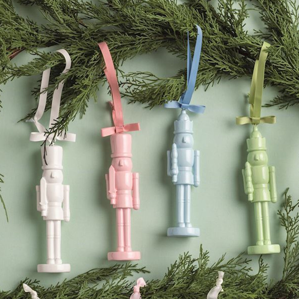 Pastel-colored lacquered nutcracker ornaments hanging on evergreen pine branches.
