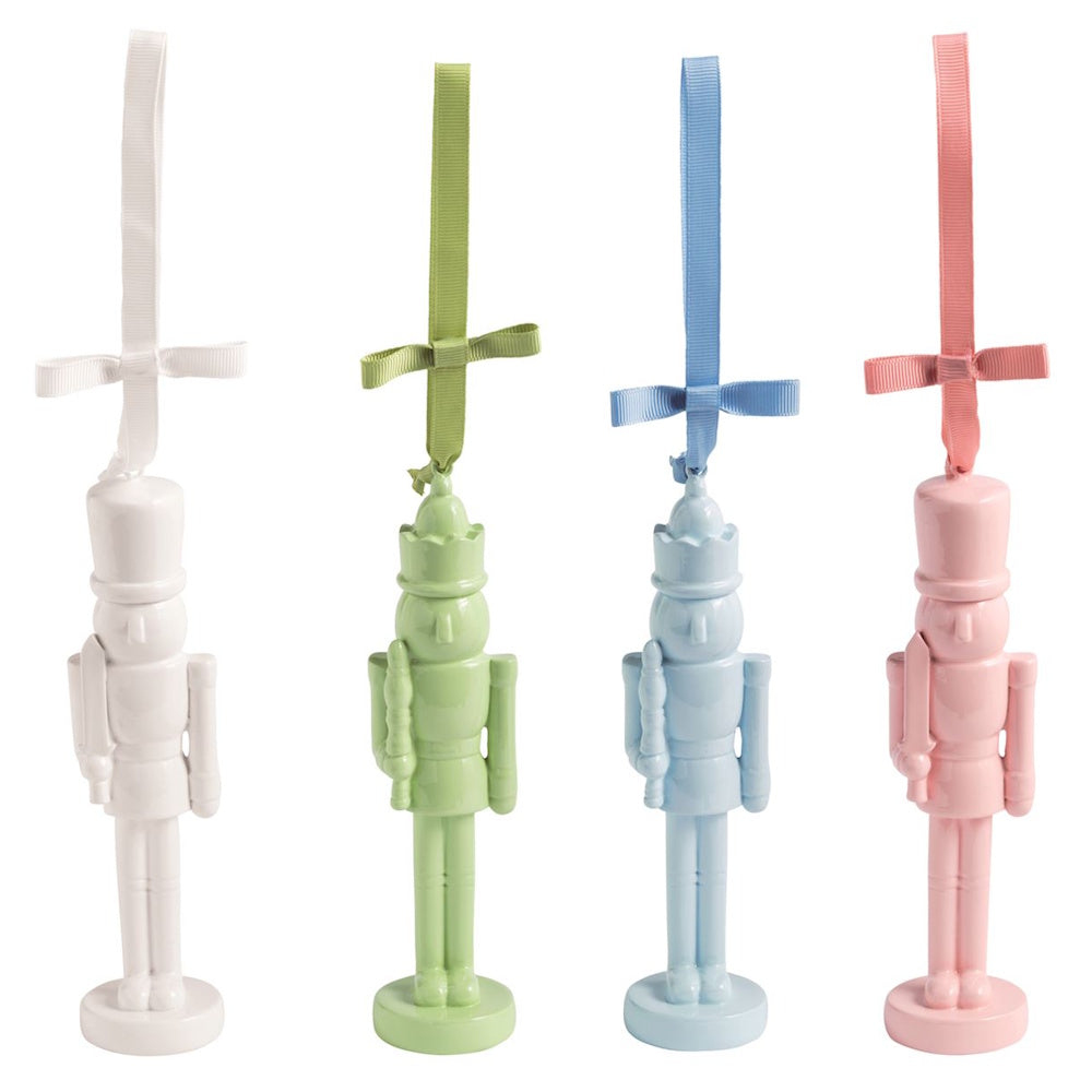 Four pastel lacquered nutcracker ornaments in white, green, blue, and pink with hanging ribbons.