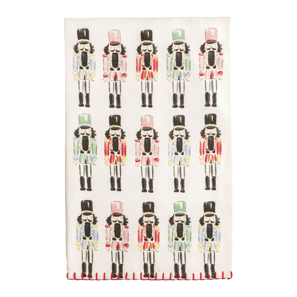 White tea towel featuring rows of colorful illustrated nutcrackers with red stitched trim.