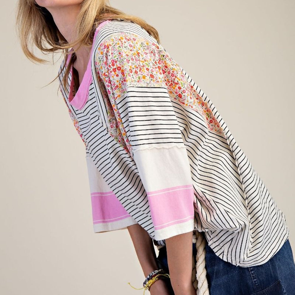 A woman in a patchwork floral and striped top bends forward.