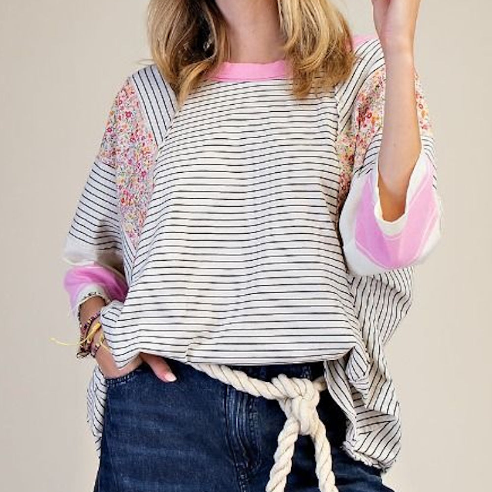 Woman in a mineral washed striped knit top with floral patchwork sleeves and pink accents, tucked into denim jeans.