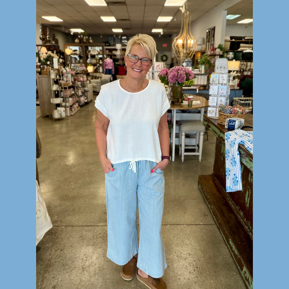 Woman in an off-white linen-blend drawstring top and blue striped wide-leg pants in a boutique home goods store.