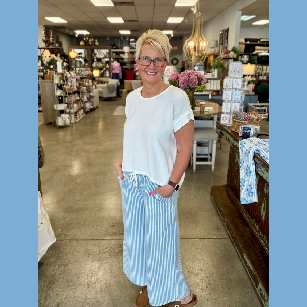 Woman in an off-white linen-blend drawstring top and blue striped wide-leg pants standing in a home decor boutique.