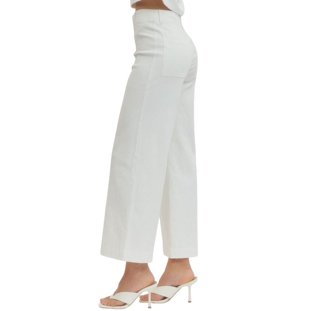 Side view of a person wearing off-white high-rise, wide-leg pants and cream heeled sandals.