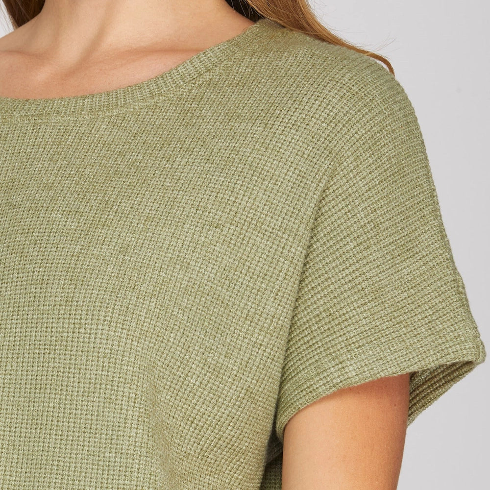 Close-up of a woman wearing an olive green round-neck knit top with relaxed drop-shoulder sleeves.