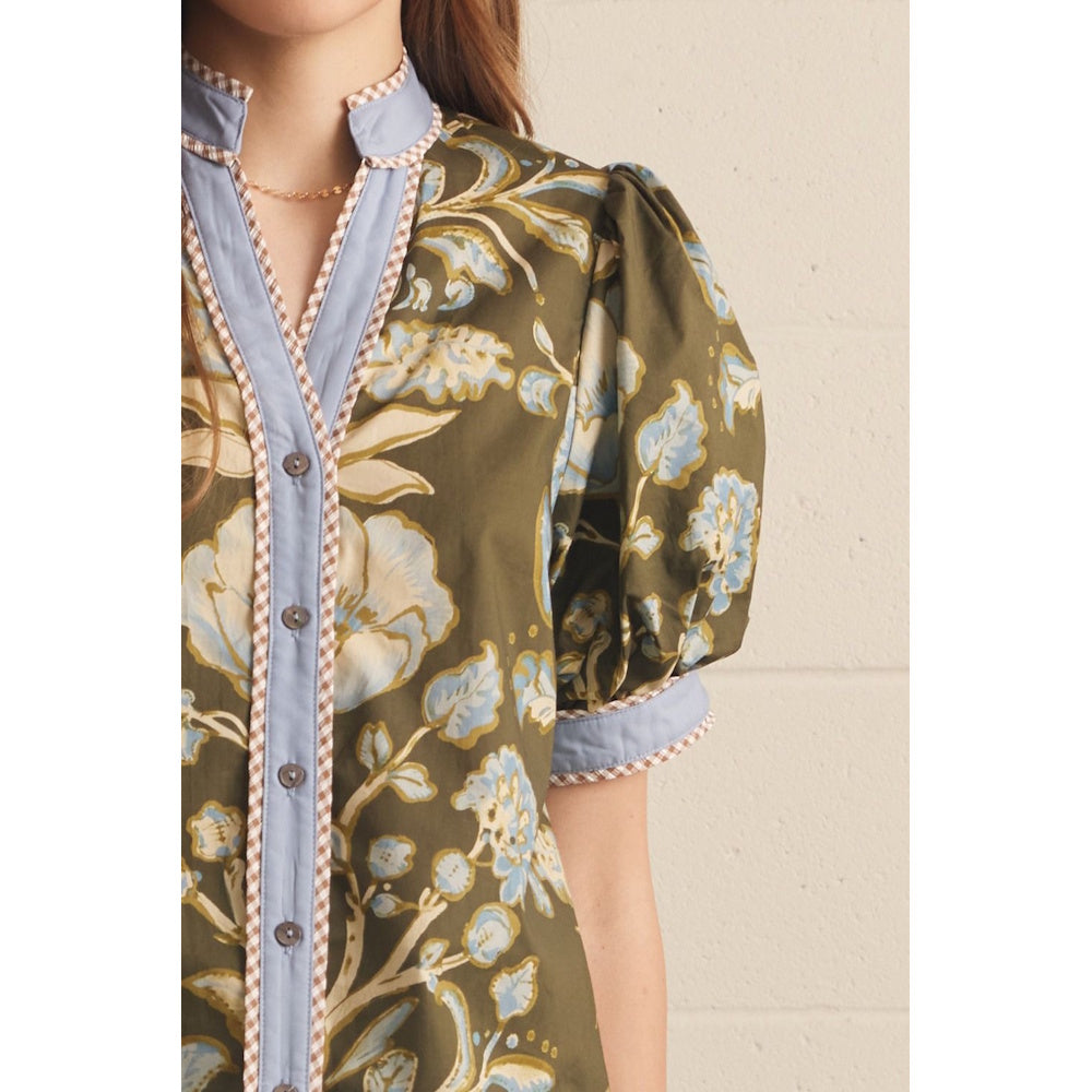 Close-up of an olive green floral top featuring a blue placket, patterned trim, and puff sleeve.