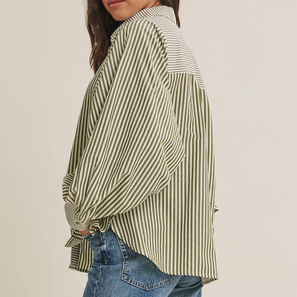 Side view of an oversized, olive green and white striped long-sleeve button-down shirt paired with jeans.