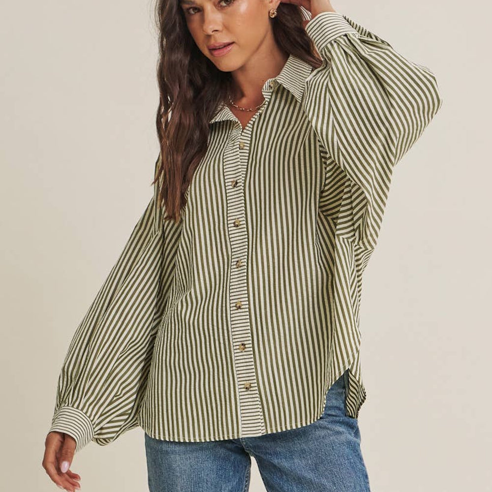 Woman wearing an olive green and white striped button-down shirt with wide batwing sleeves and jeans.