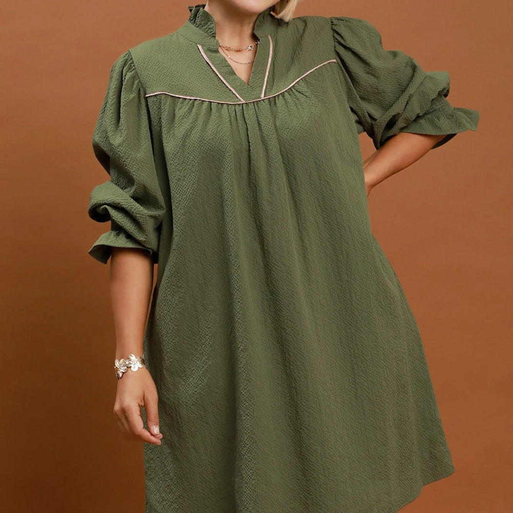 Textured olive green mini dress featuring puff sleeves, a ruffled collar, and pink trim accents.