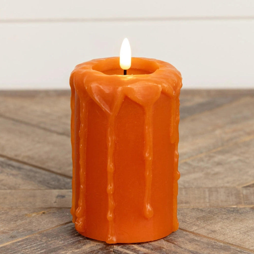 Lit orange pillar candle with wax drips sitting on a wooden surface.