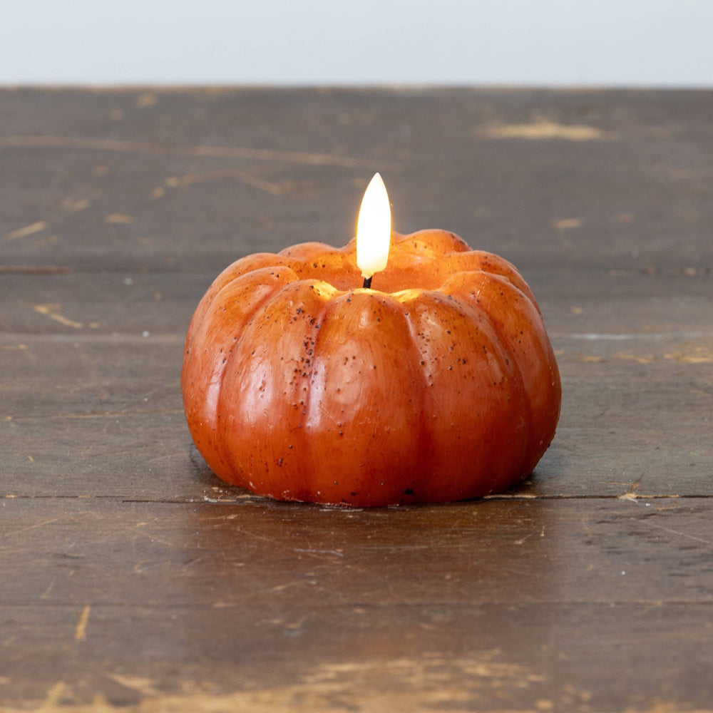 Short, orange pumpkin-shaped flameless candle with a warm LED light resting on a rustic wooden surface.