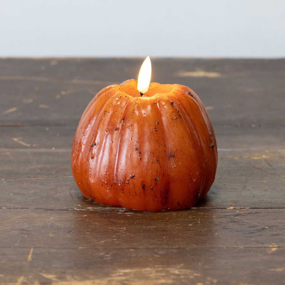 A rustic orange pumpkin-shaped candle with a glowing flame resting on a weathered wooden surface.