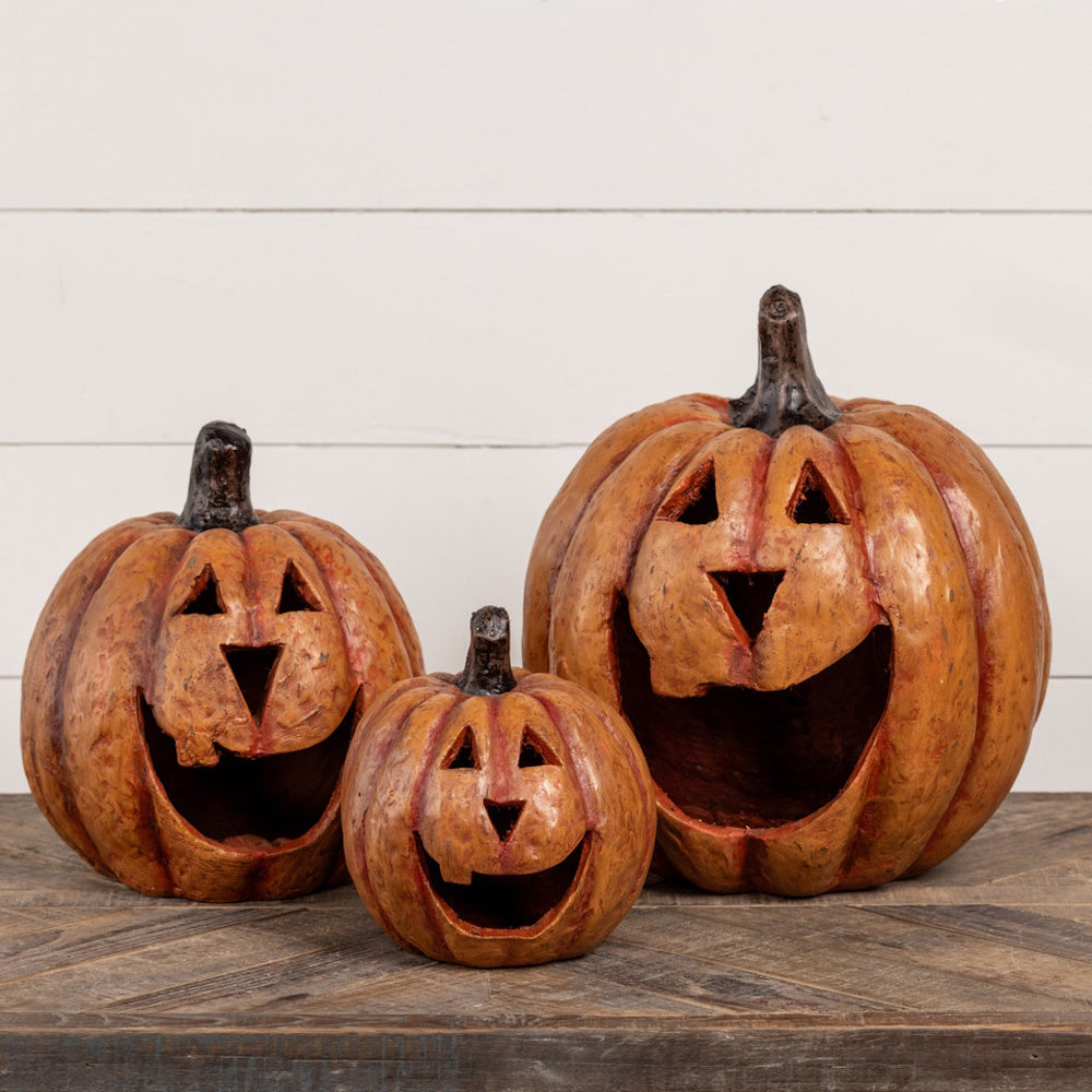 Three carved jack-o'-lantern pumpkins with wide smiling mouths arranged on a wooden surface.