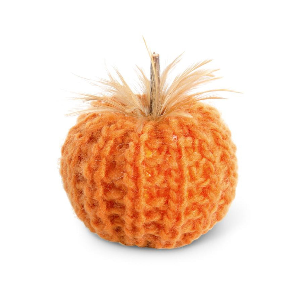 Orange crochet pumpkin figure topped with a wooden stem and feathery accents.