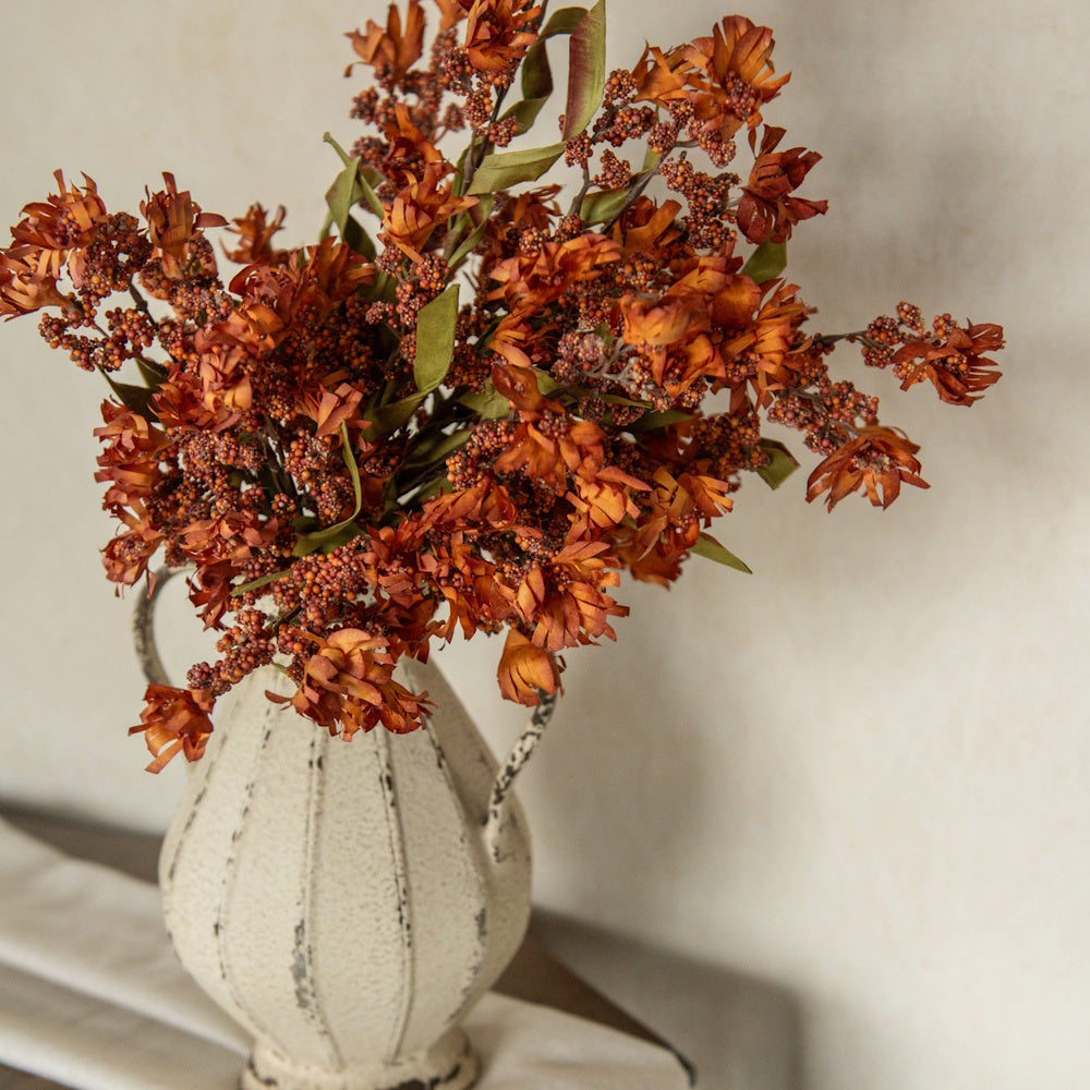 Orange mini berry wildflower arrangement in a rustic textured white ceramic vase.