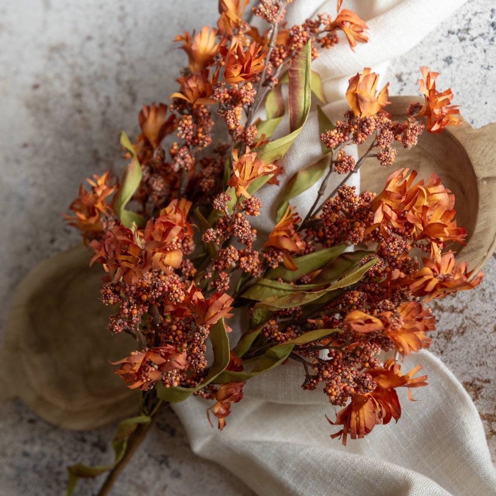 Faux orange mini berry wildflower bush stems on white linen cloth for rustic autumn decor.