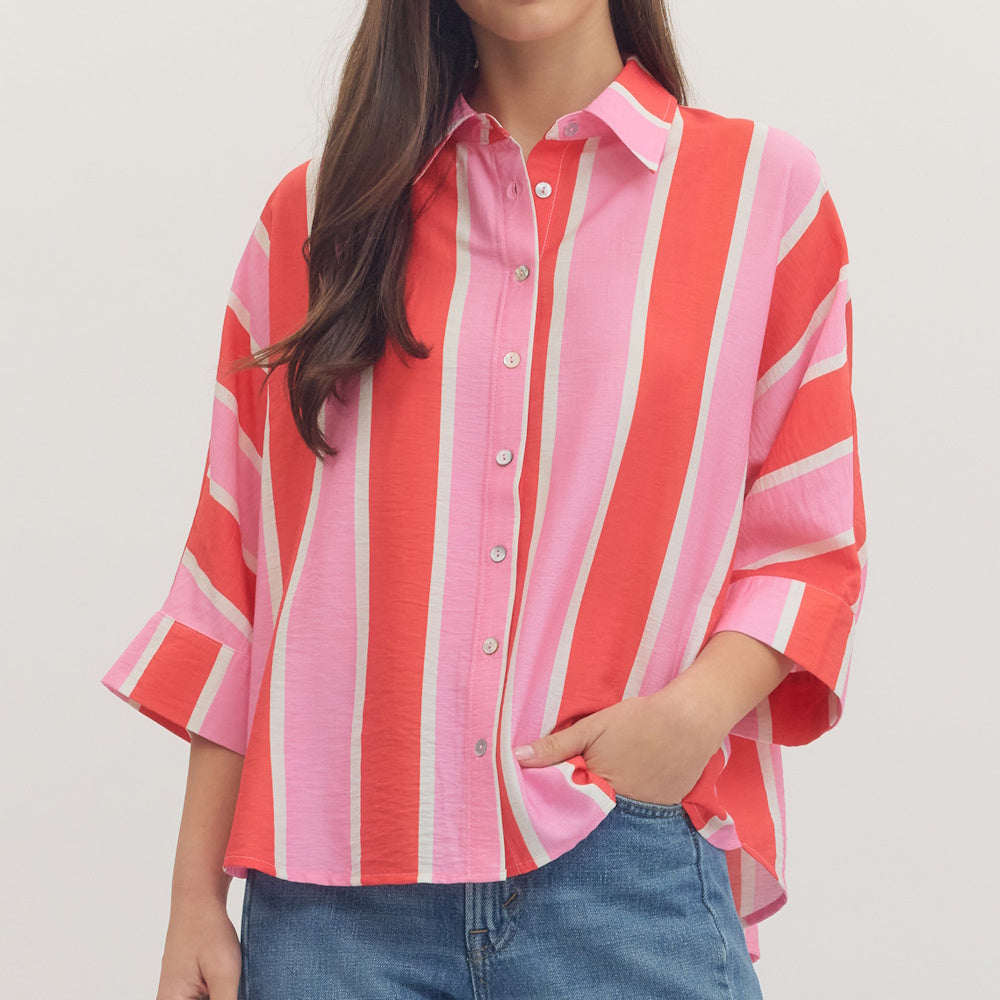 A woman wearing a vibrant pink, orange, and white vertically striped button-down shirt with blue jeans.