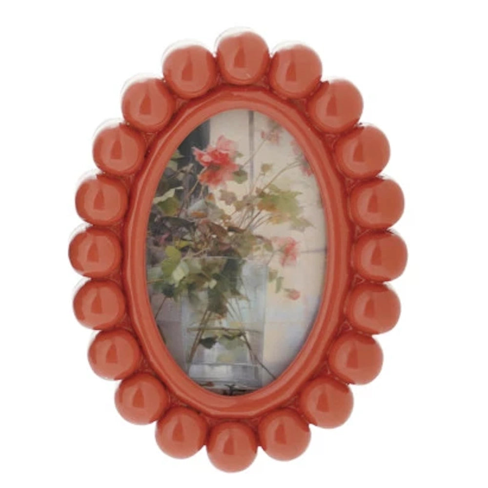 Small oval orange resin photo frame with a beaded ball border, featuring a picture of pink flowers in a glass vase.
