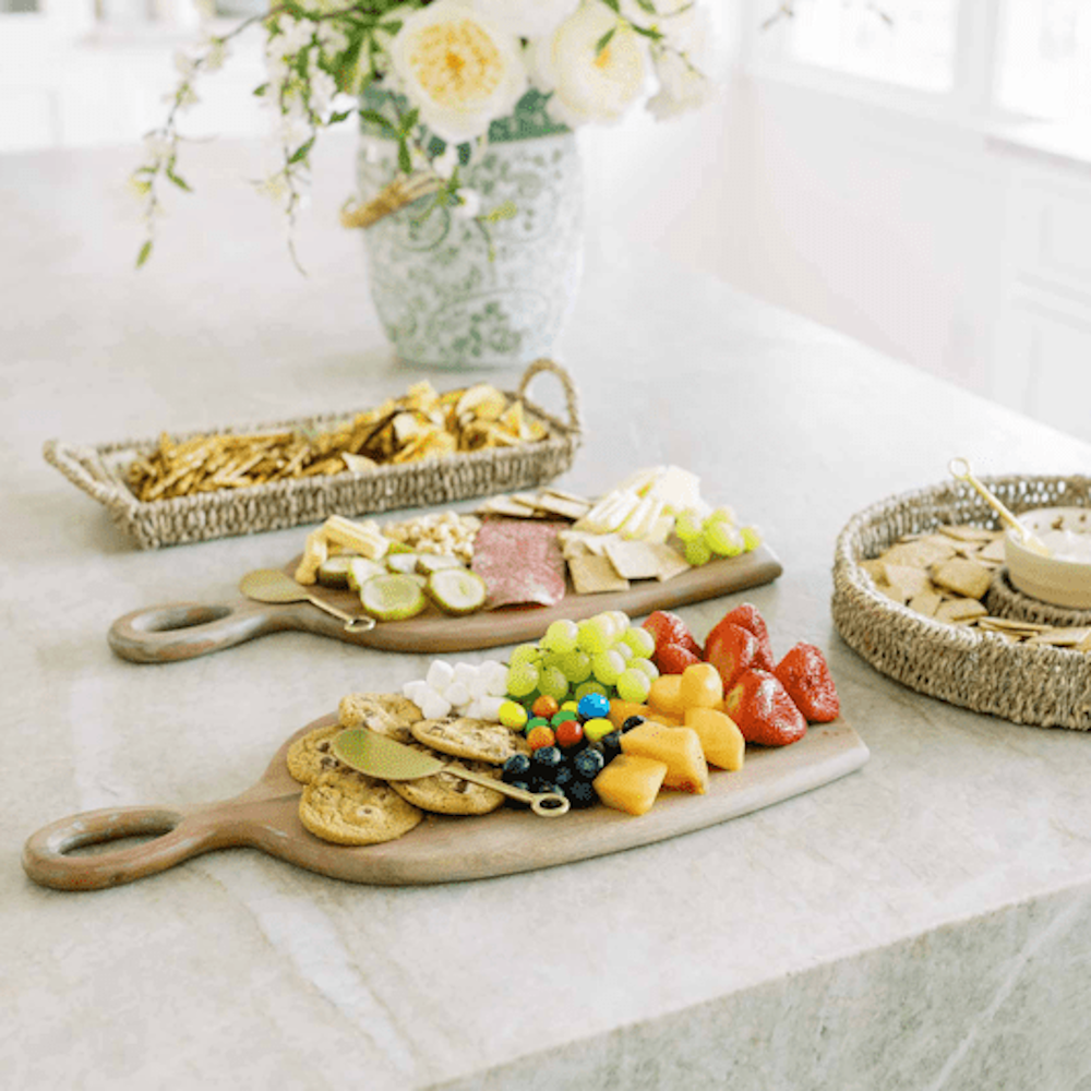 A spread of snacks, fruit, and sweets arranged on wooden serving boards and woven baskets on a counter.