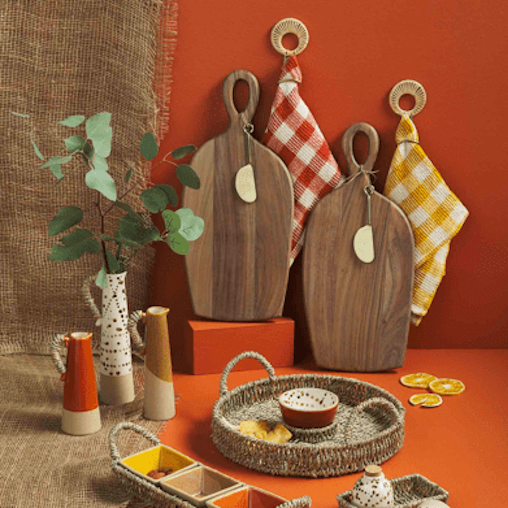 A rustic kitchen display with wooden cutting boards, checkered towels, woven trays, and ceramic pitchers.