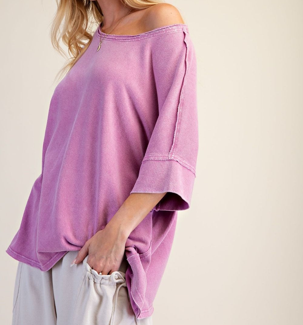 Side profile of a woman wearing an oversized pink washed terry knit top with raw-edge seam details.