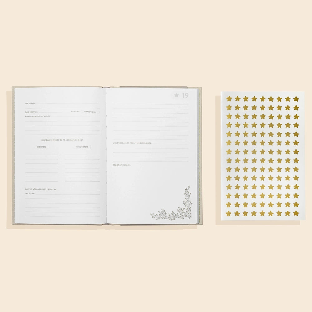 Open bucket list journal for couples with guided prompts next to a sheet of gold star stickers on a cream background.