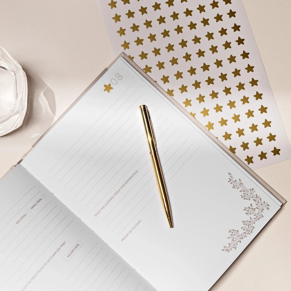 Open bucket list journal for couples with a gold pen and star stickers on a desk.