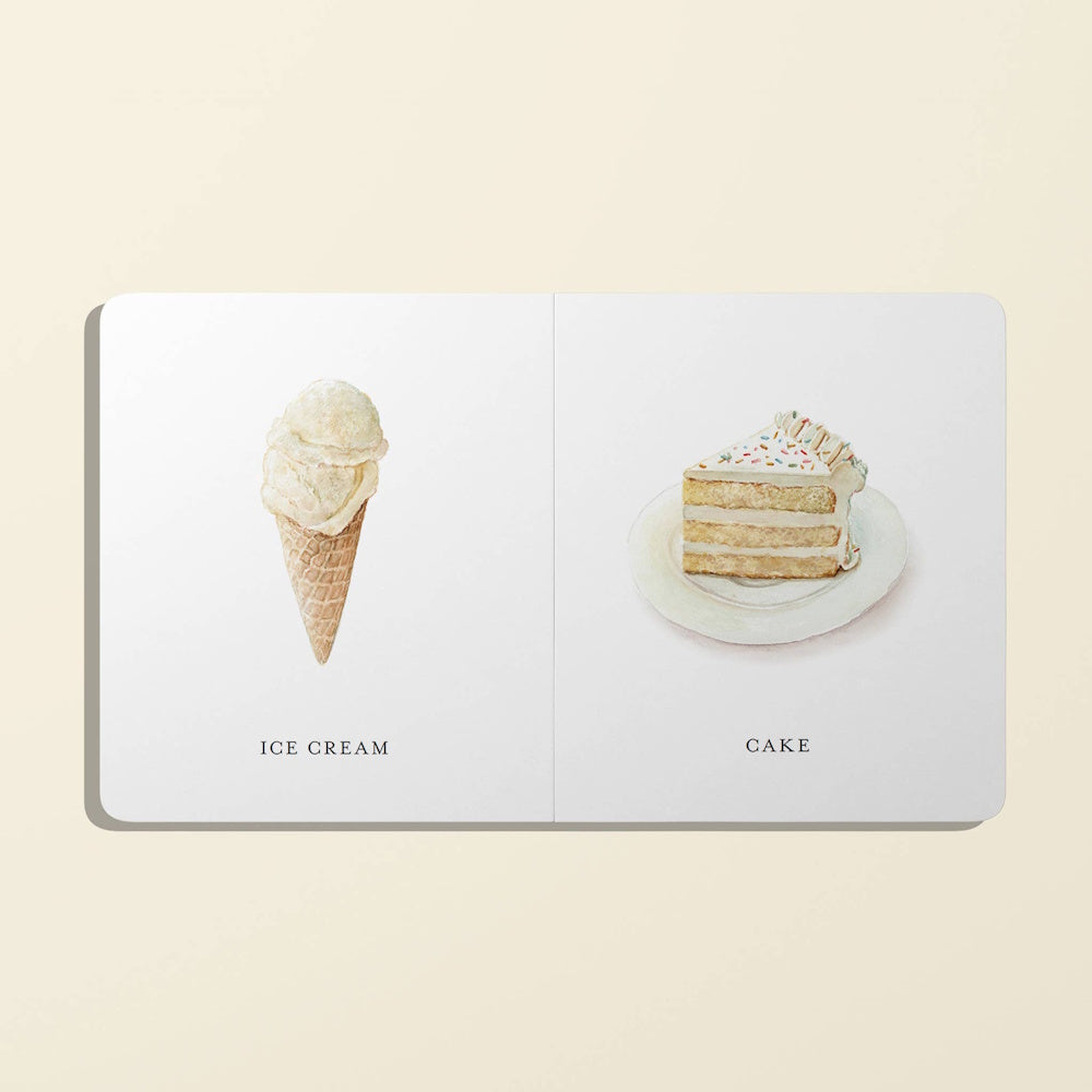 An open children's board book showing simple illustrations of an ice cream cone and a slice of sprinkle cake.