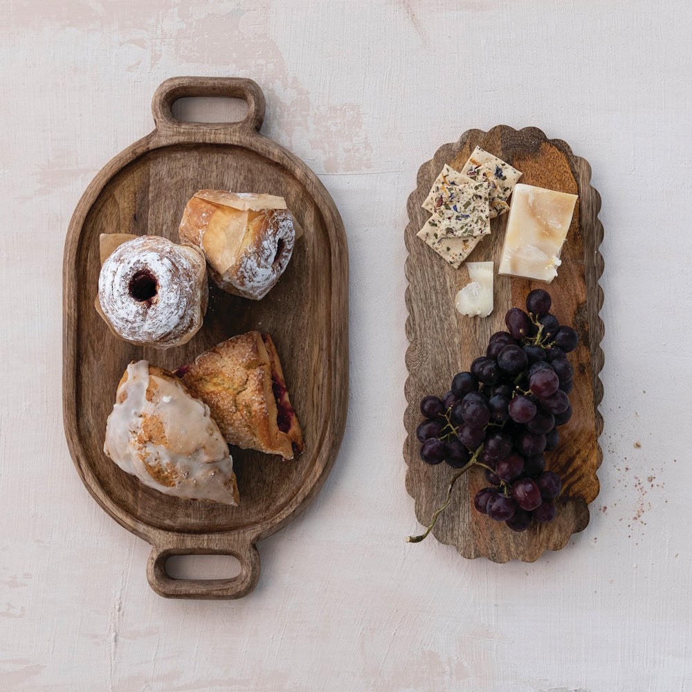 Flat lay of pastries on an oval wooden tray next to cheese, crackers, and grapes on a scalloped board.