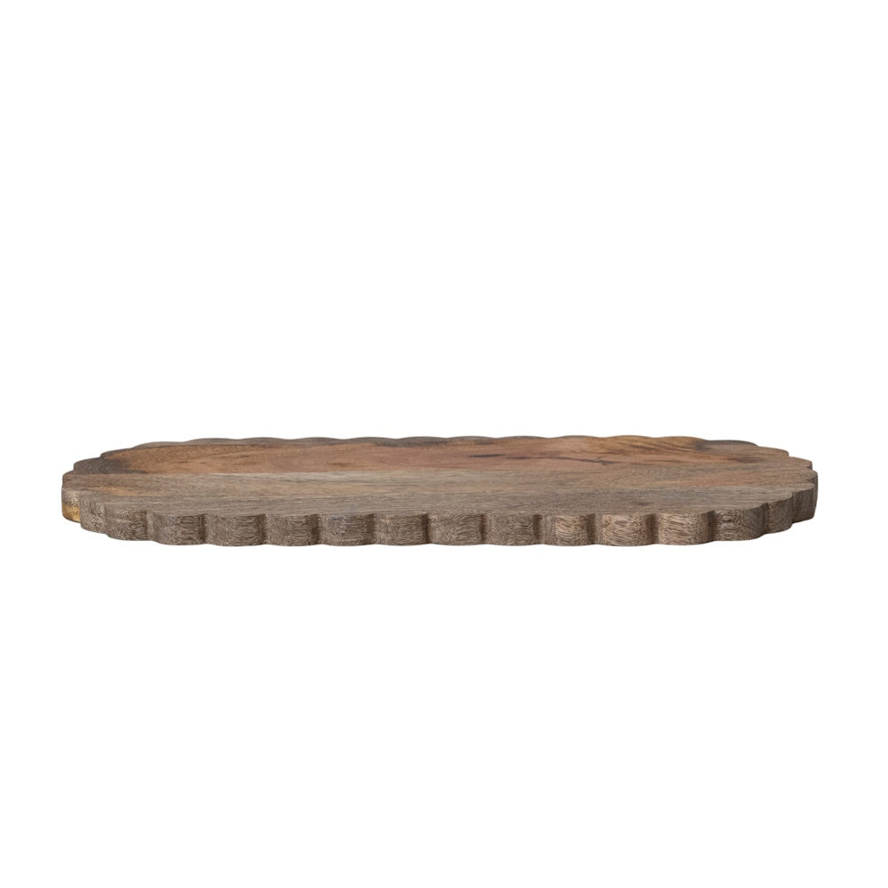 Side view of a flat, oval wooden serving board featuring a distinctive scalloped edge and natural grain.