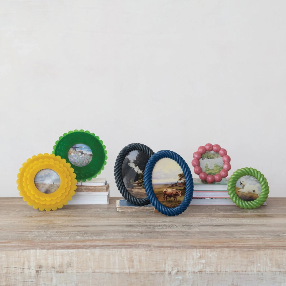 Six colorful, textured resin picture frames in various shapes and sizes displayed on a wooden shelf with books.