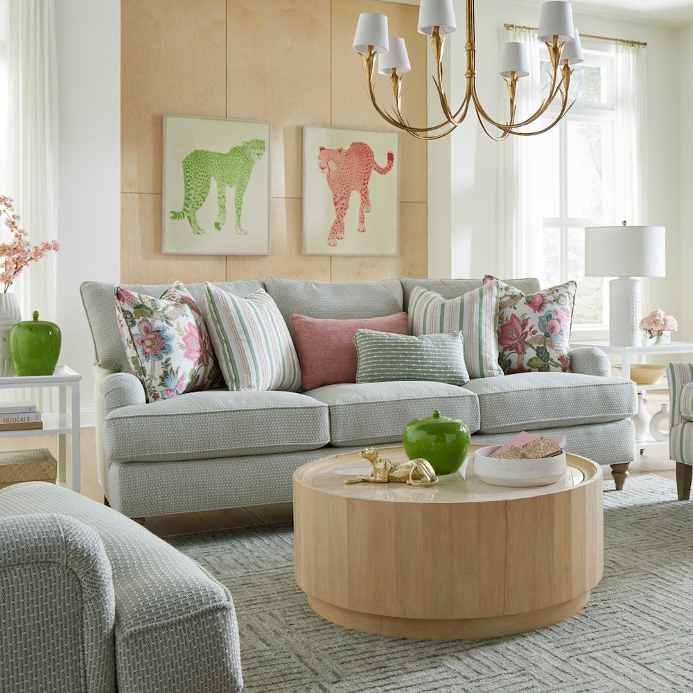 Light grey textured three-cushion sofa styled with floral and striped accent pillows in a bright living room.