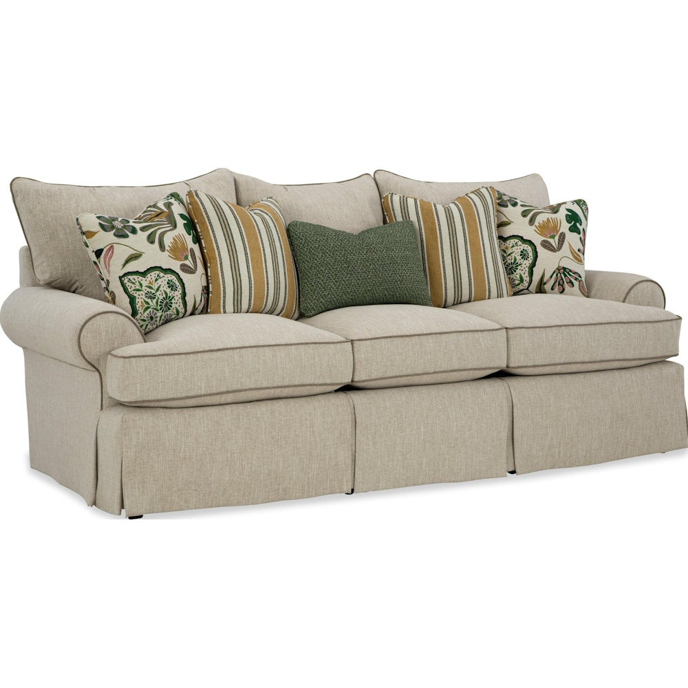 Beige skirted three-cushion sofa styled with striped and floral accent pillows against a white background.