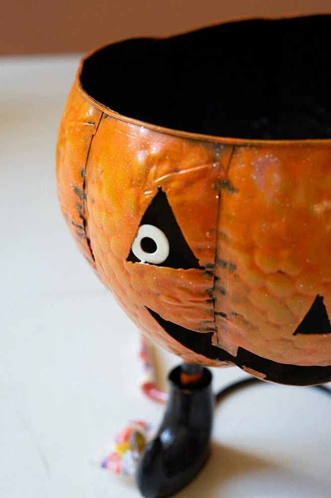 Painted orange metal jack-o'-lantern candy bowl with a cutout eye and a small black boot.