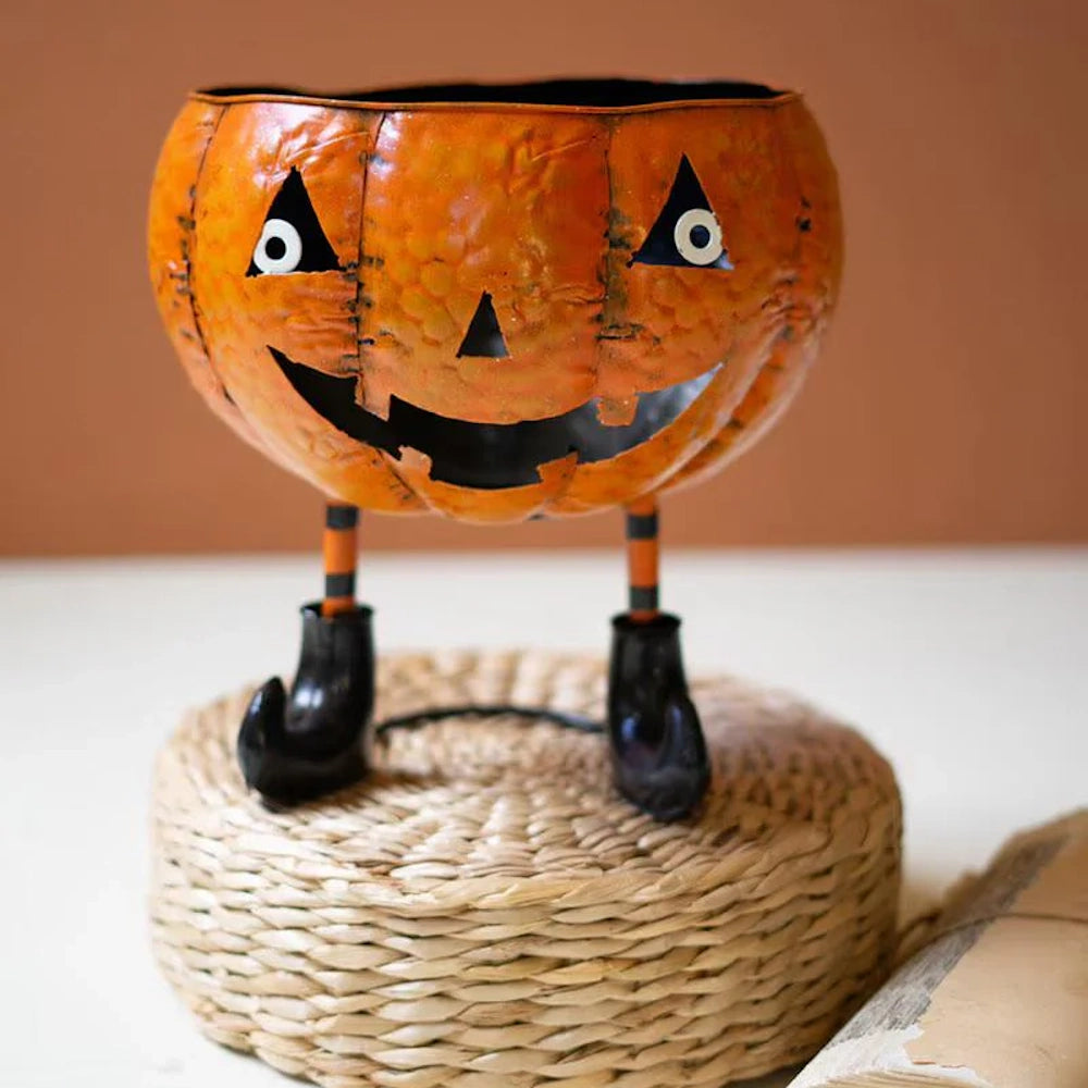 Painted metal Jack-o'-lantern candy bowl with striped legs and witch boots on a woven base.