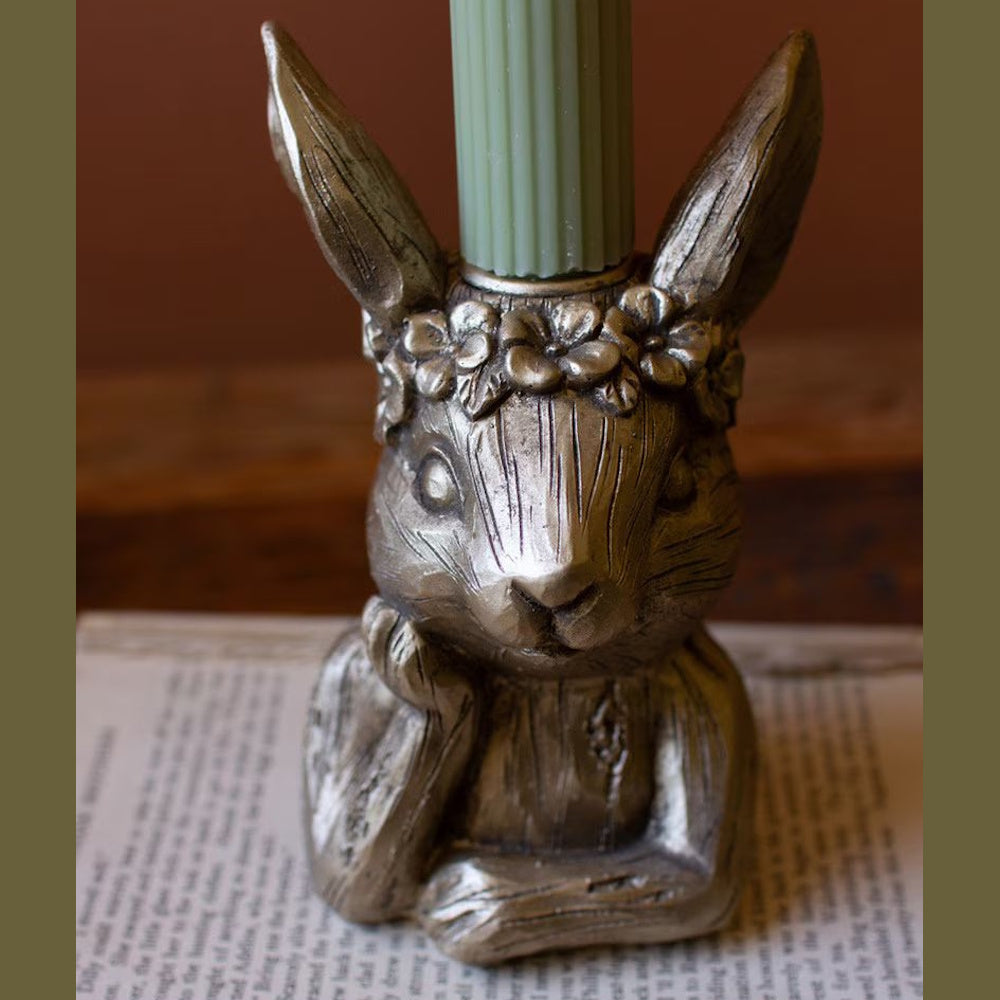 Gold resin rabbit taper candle holder with a floral crown, holding a green ribbed candle over an open book.
