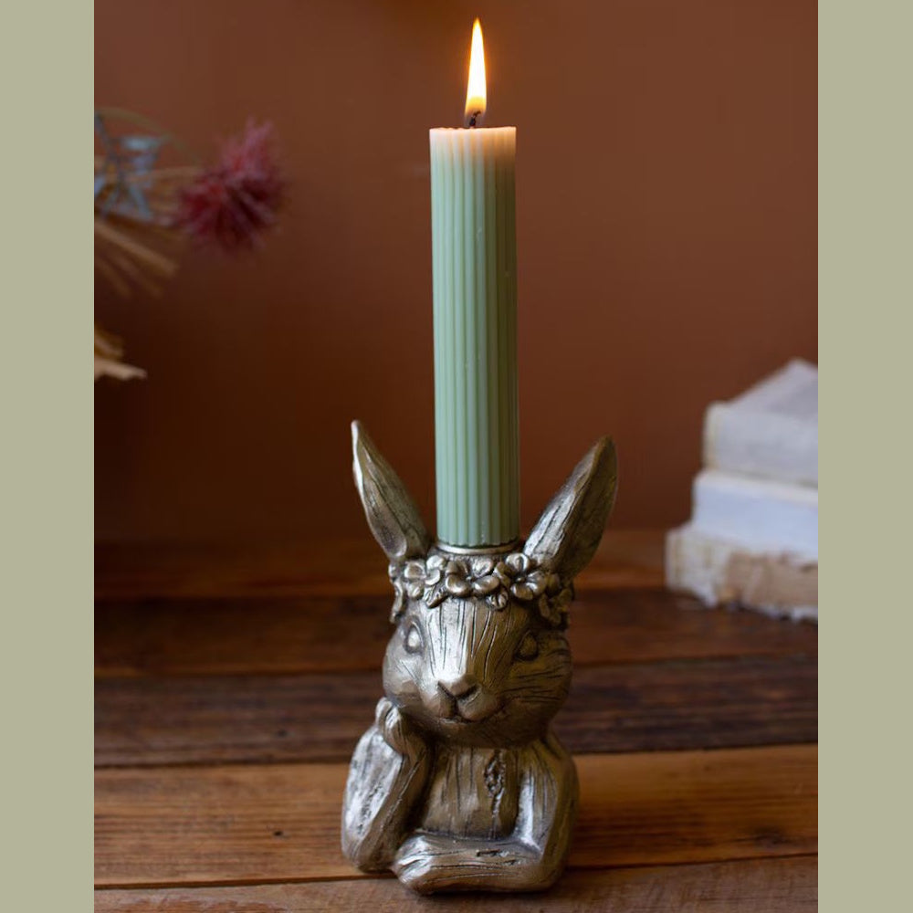 A metallic gold rabbit candle holder wearing a flower crown, holding a lit green fluted taper candle.