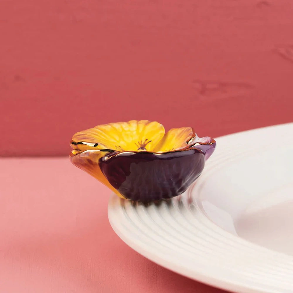 A yellow and purple ceramic pansy-shaped decorative piece attached to the rim of a white plate.