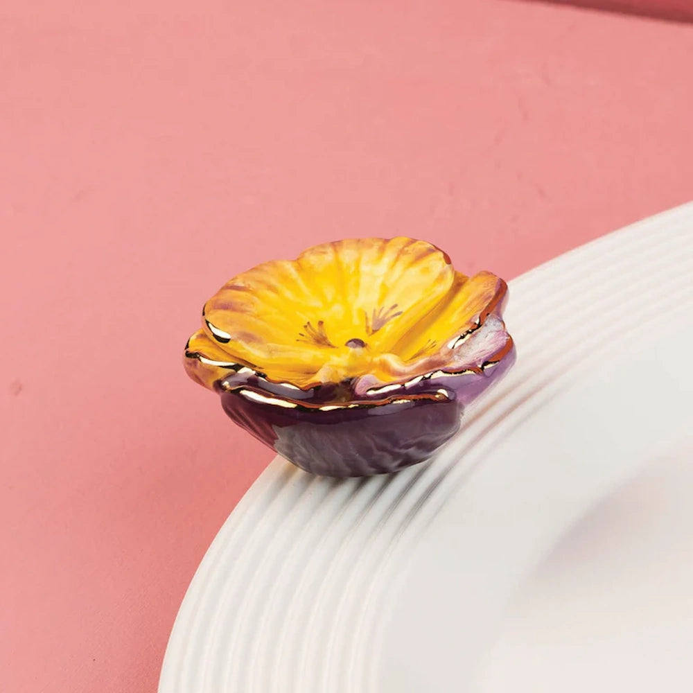 Yellow and purple ceramic pansy flower accent with gold trim resting on the edge of a white plate.