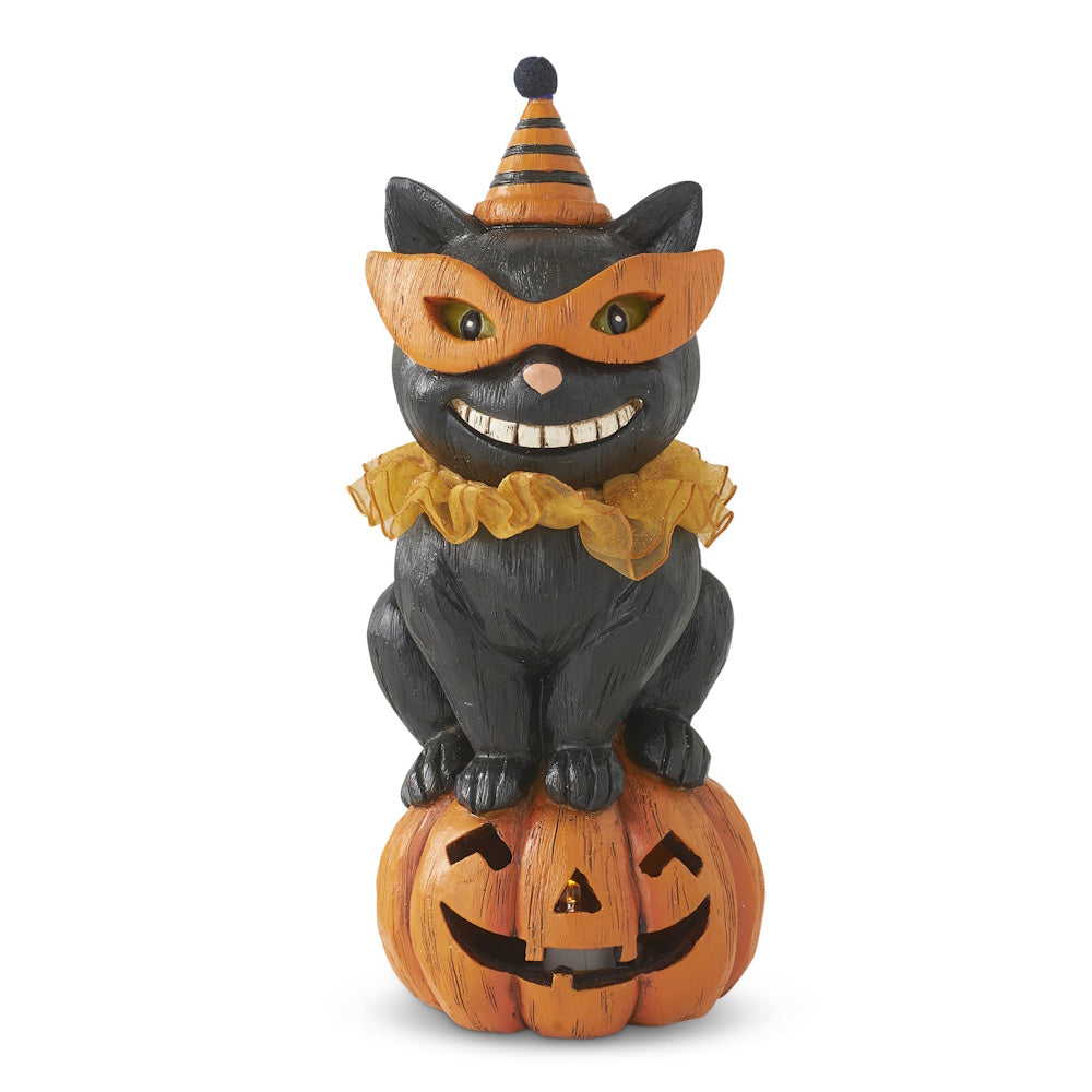 Halloween decoration of a smiling black cat wearing a mask and party hat, sitting on a jack-o'-lantern.