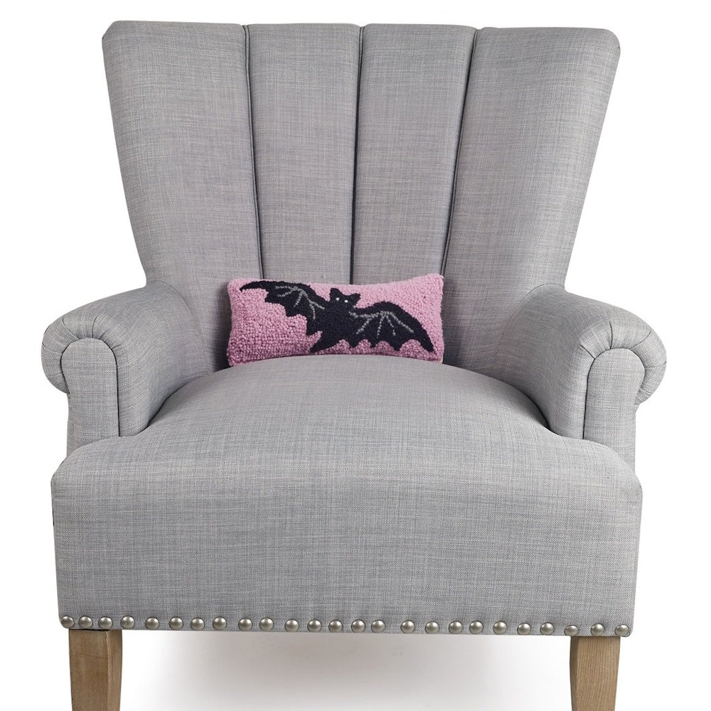 Pink hooked pillow featuring a black bat design sitting on a grey armchair.