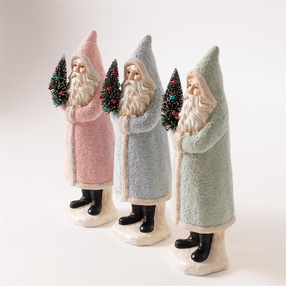 Three vintage-style Santa figurines in pastel pink, blue, and green robes holding mini trees.