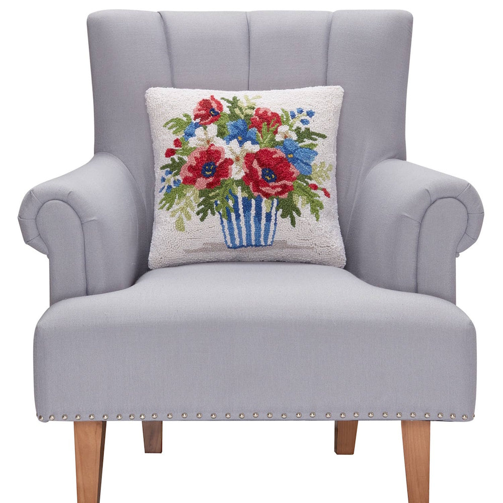 Patriotic red poppy hooked pillow with blue striped vase on a gray upholstered armchair with wood legs.