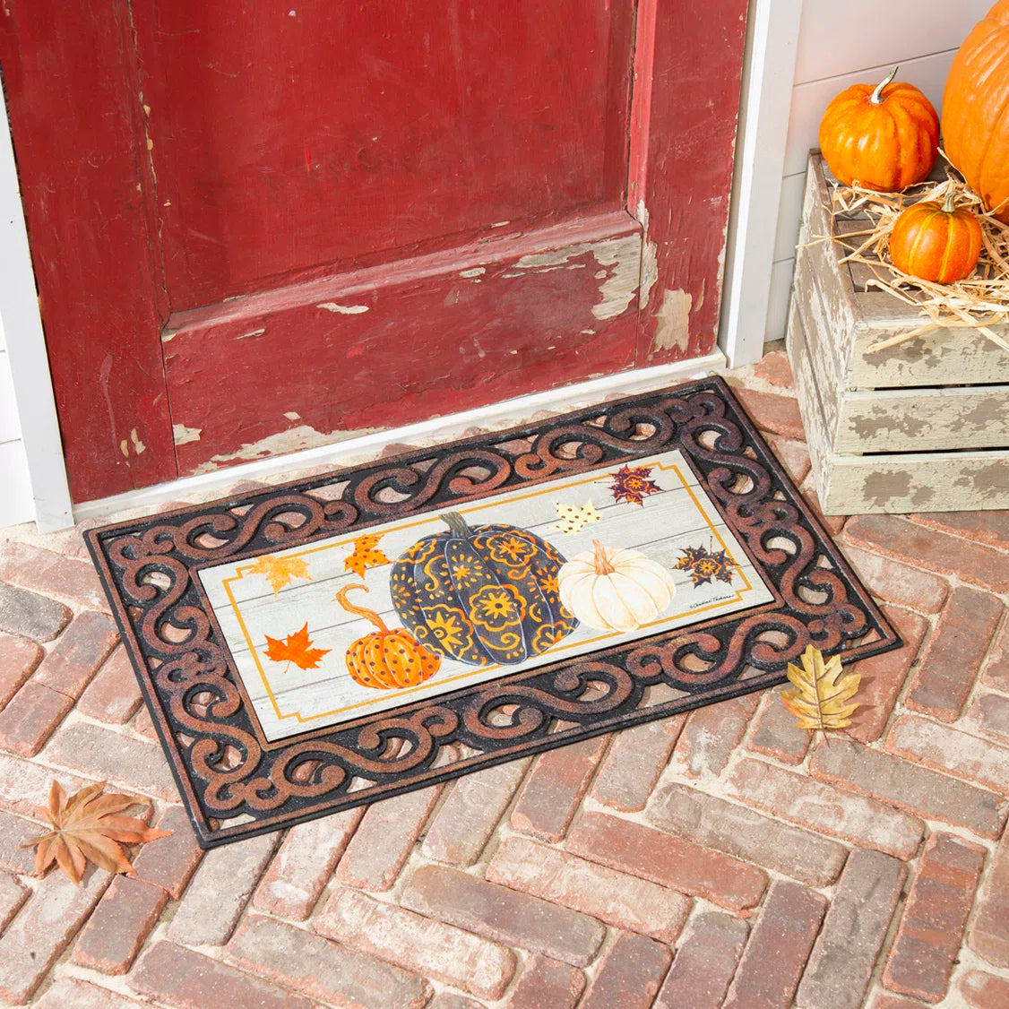 Autumn doormat featuring patterned pumpkins and leaves set outside a rustic red front door.